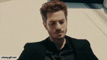 a man in a black suit and black shirt is sitting on the ground .