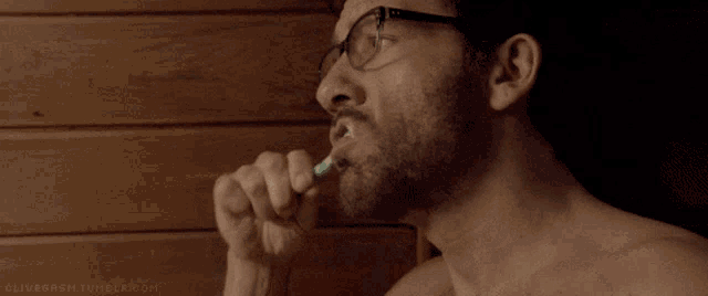 a shirtless man brushes his teeth with a green toothbrush