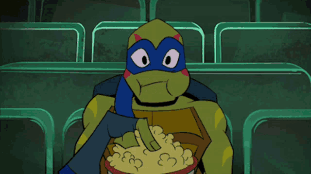 a teenage mutant ninja turtle is eating popcorn in a theater