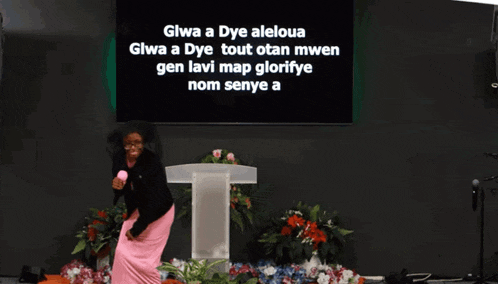 a woman stands in front of a podium with the words gwa a dye aleloua written on the screen behind her