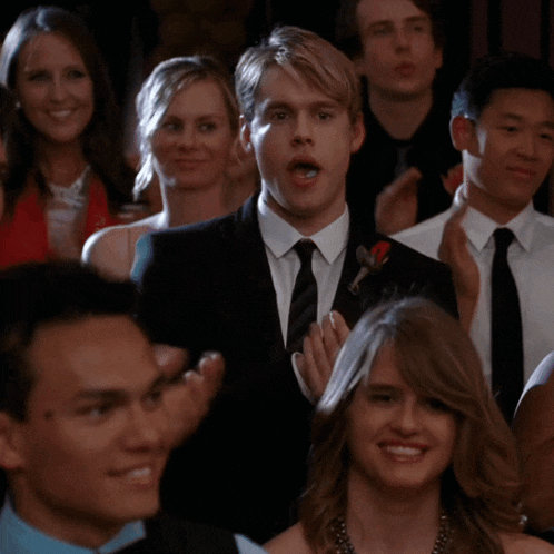 a man in a suit and tie stands in a crowd of people applauding
