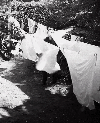 a black and white photo of a person hanging laundry on a clothes line .
