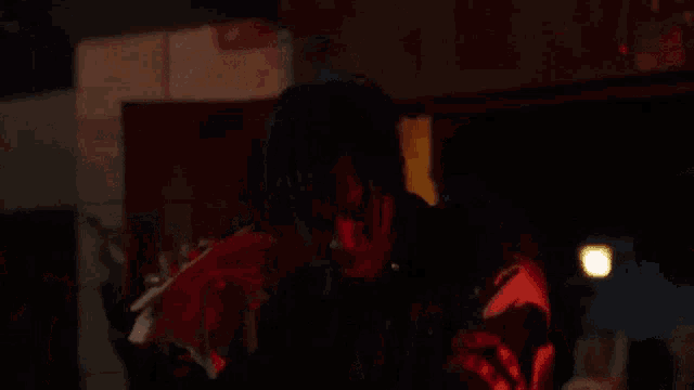 a man in a black jacket is standing in a dark room with a red light behind him .
