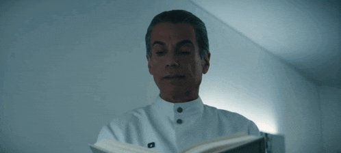 a man in a white coat reads a book with his eyes closed