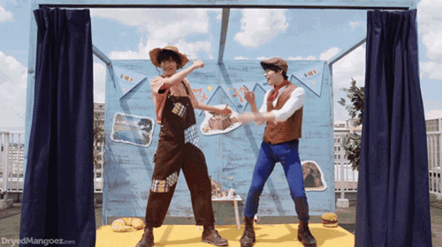 two men dancing in front of a sign that says ' dryedmangoez.com '