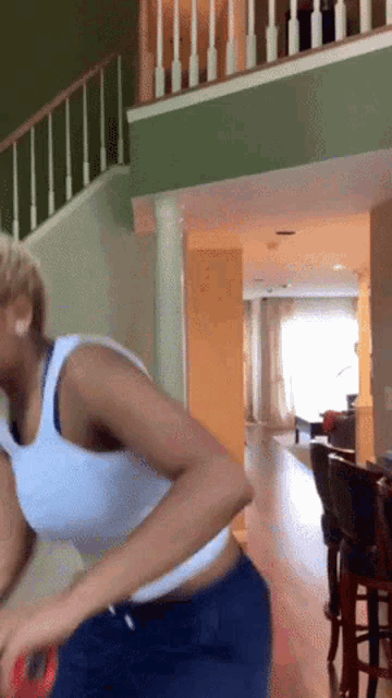 a woman in a white tank top and blue shorts is standing in a living room