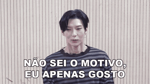 a young man wearing a striped shirt is standing in front of a wall and says não sei o motivo