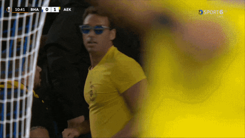 a man wearing sunglasses and a yellow shirt stands in front of a goal during a soccer game