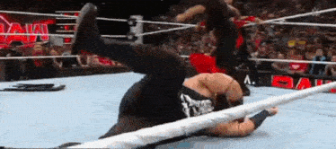 a wrestler is laying on the ground in a wrestling ring while another wrestler kicks him .