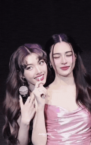 two women are standing next to each other and one is holding a microphone .