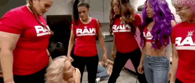 a group of women in red shirts are standing around a woman in a room .