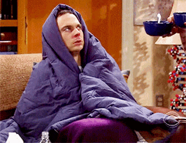 a man wrapped in a purple blanket sits on a couch