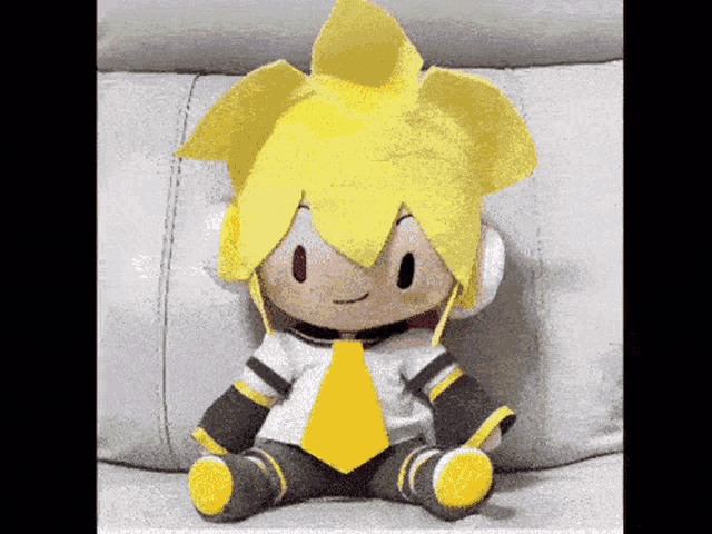 a stuffed doll with yellow hair and a yellow tie is sitting on a white couch .