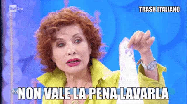 a woman in a yellow jacket is holding a piece of paper with the words non vale la pena lavarla below her