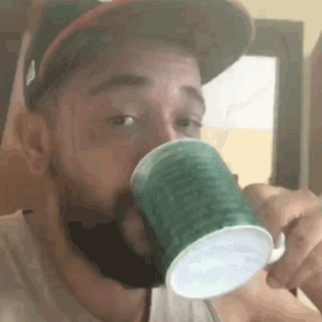 a man with a beard is drinking from a green cup with a straw .