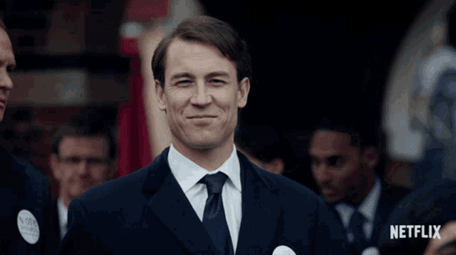 a man in a suit and tie is smiling with a netflix logo behind him