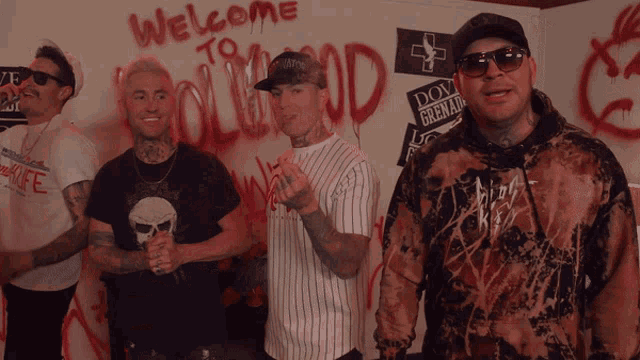 a group of men stand in front of a wall that says welcome to hollywood
