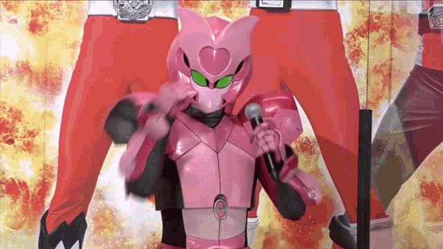 a pink robot with green eyes is holding a microphone in front of a man in red pants