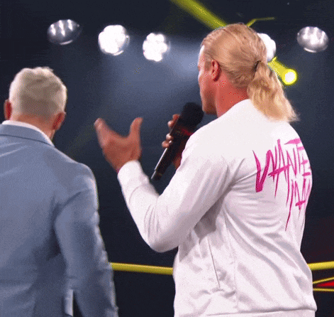 a man wearing a white jacket with a pink lettering on the back holds a microphone