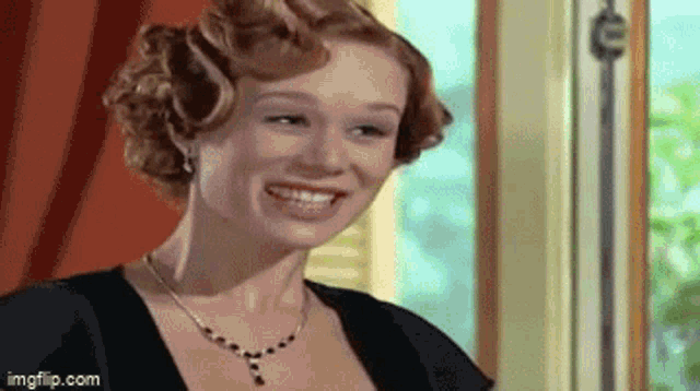 a woman in a black dress and necklace is smiling .