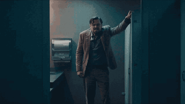 a man leaning against a wall in a bathroom with a paper towel dispenser
