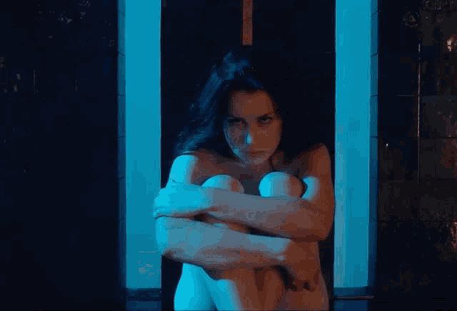 a naked woman is sitting in a doorway with her arms around her knees