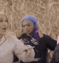a woman with purple hair is pointing at another woman 's face .