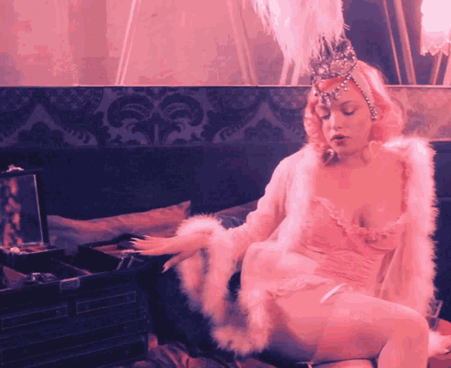 a woman with pink hair and feathers on her head sits on a couch