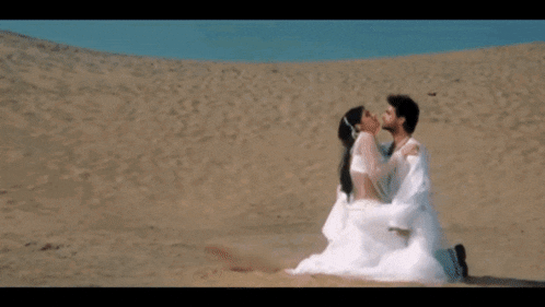 a man is holding a woman in his arms in the sand .