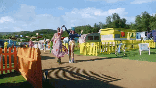 two women are dancing in front of a yellow fence and a yellow trailer