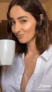 a woman wearing a white shirt is holding a cup of coffee .