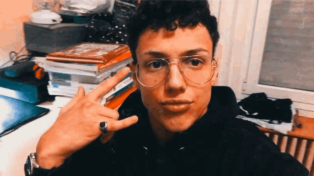 a young man wearing glasses and a ring is giving a peace sign