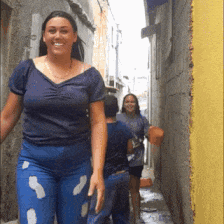 a woman in a blue shirt is walking down an alleyway
