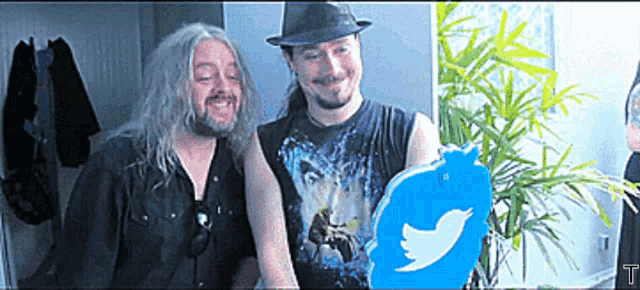 two men are standing next to each other and one of them is holding a twitter logo