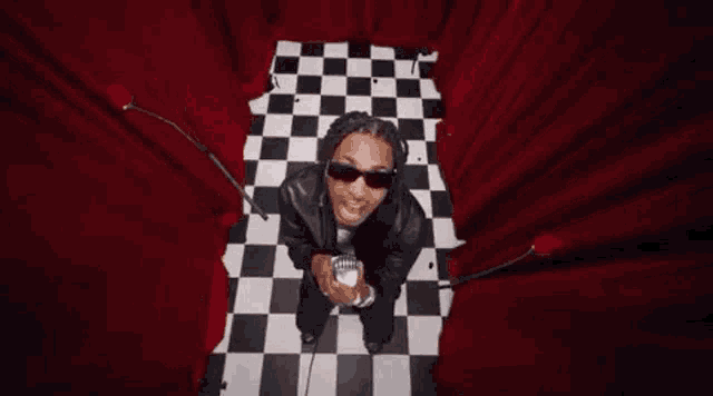 a man wearing sunglasses is holding a microphone in a room with checkered floors .