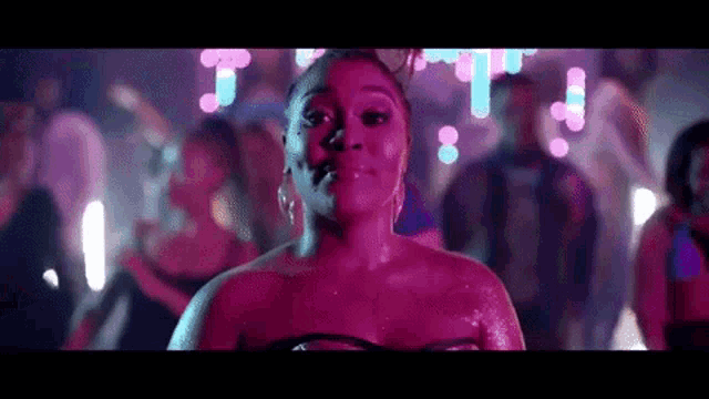 a woman in a pink dress is standing in front of a crowd of people dancing at a party .