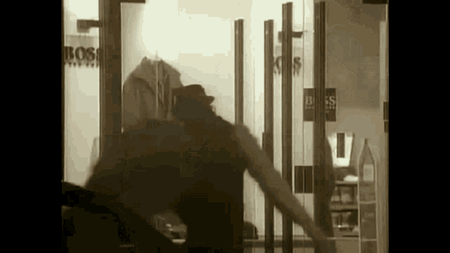 a black and white photo of a man in a hat standing in front of a store window .