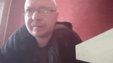 a man wearing glasses and a black jacket is sitting at a table looking at the camera .