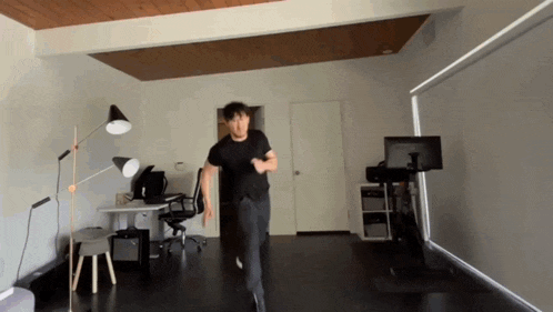 a man in a black shirt is running in a room with a desk and chair