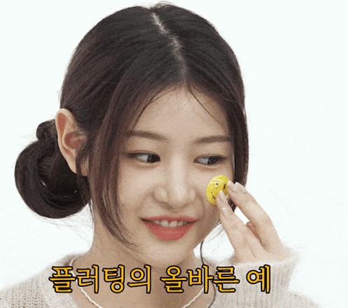 a woman is holding a yellow object on her face with korean writing behind her