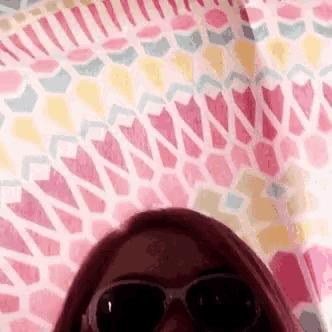 a woman wearing sunglasses is standing in front of a pink and yellow blanket .