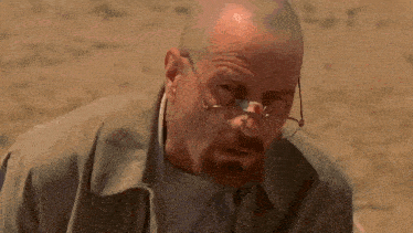a bald man with glasses and a beard is kneeling down in the dirt .