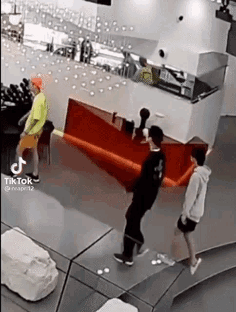a group of people are standing around a red counter in a room with a tik tok logo on the bottom right corner .