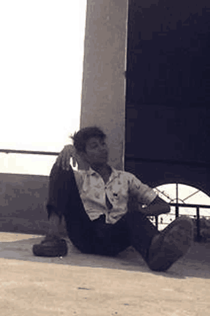 a young man is sitting on the ground with his legs crossed and smoking a cigarette .