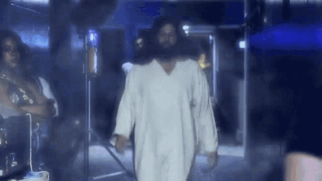 a man in a white robe with a beard is standing in a dark room