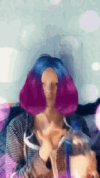 a girl with purple and blue hair is sitting on a bed
