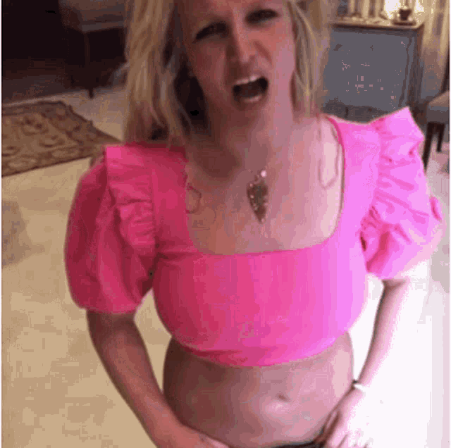 a woman in a pink top is making a funny face while holding her belly .
