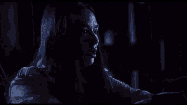 a woman with long hair is sitting in a dark room looking at a cell phone .