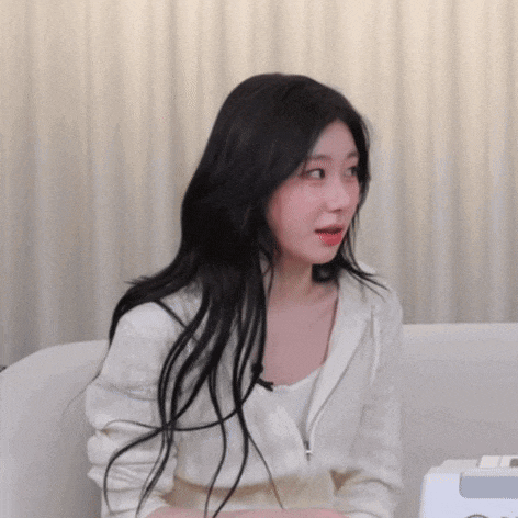 a woman with long black hair is sitting on a couch with her mouth open