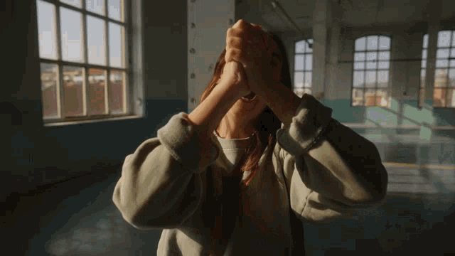 a woman in a green sweatshirt holds her hands up in front of her face